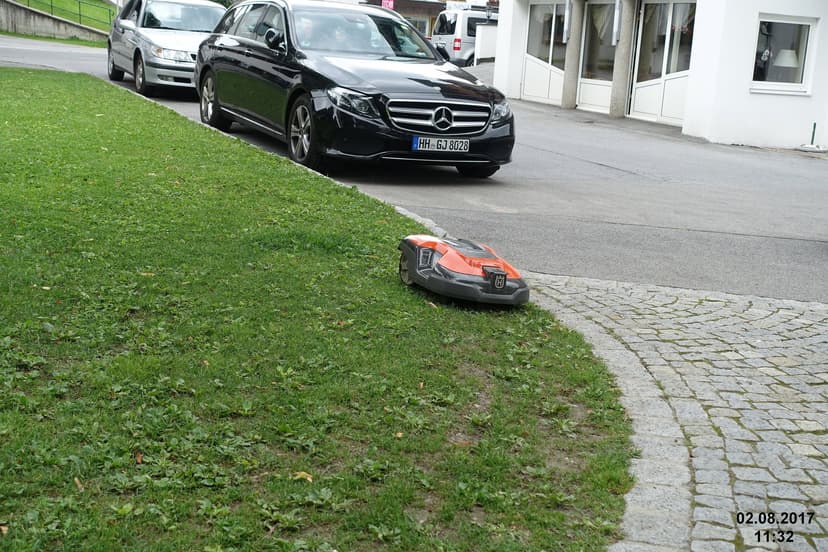 Robot mower working on a steep roadside lawn next to a driveway