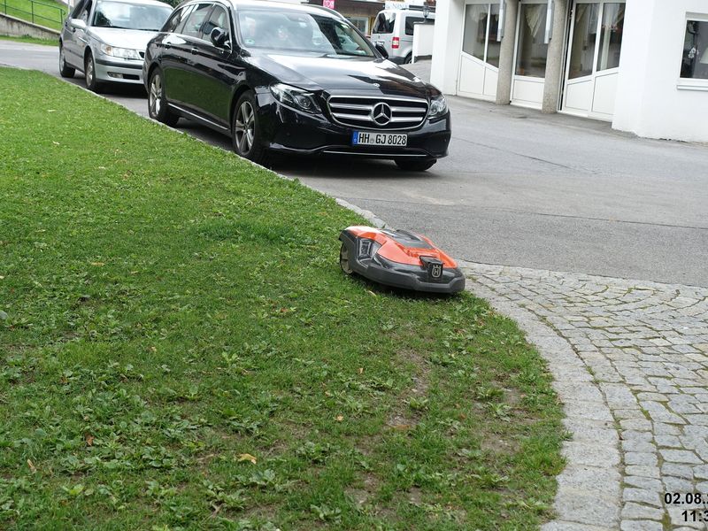 Robot mower working on a steep roadside lawn next to a driveway