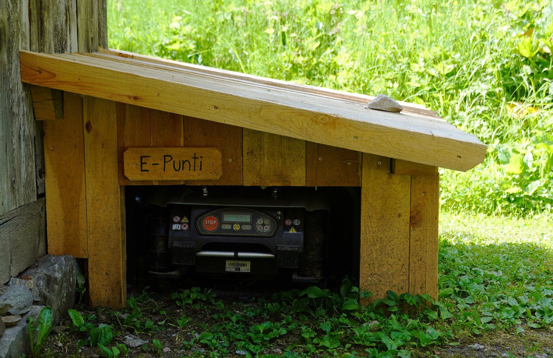 Robot mower parked inside a wooden mower garage at the edge of a lawn