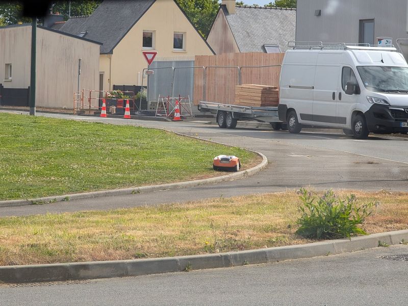 Robotic lawn mower working on a public roundabout in daylight